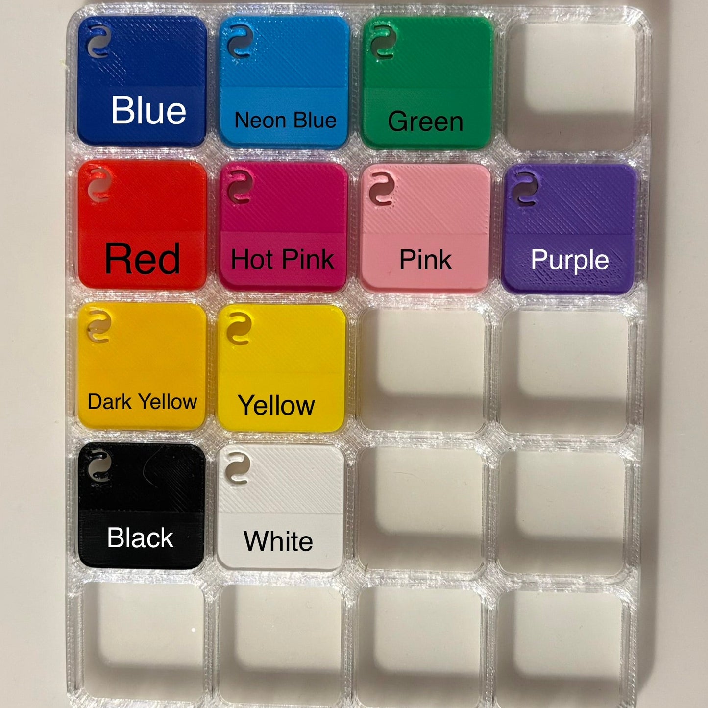 A 16-piece plastic tag tray with 4x4 slots, showing 12 colorful sample tags labeled with colors like Blue, Red, Pink, Yellow, Black, and White, alongside empty slots.